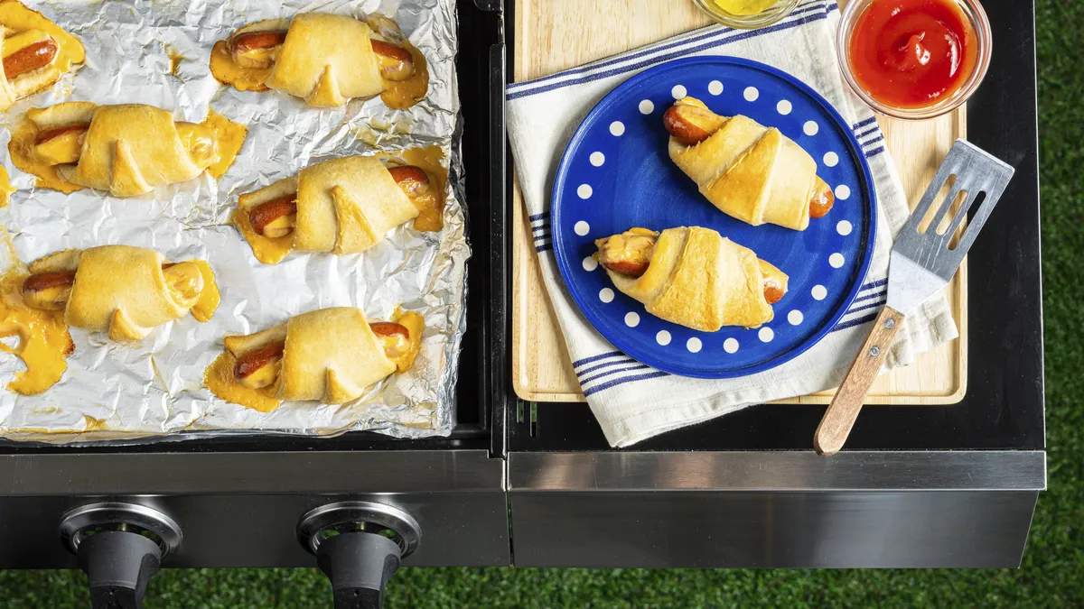 Three crescent rolls with hot dogs and melted cheese on foil.
