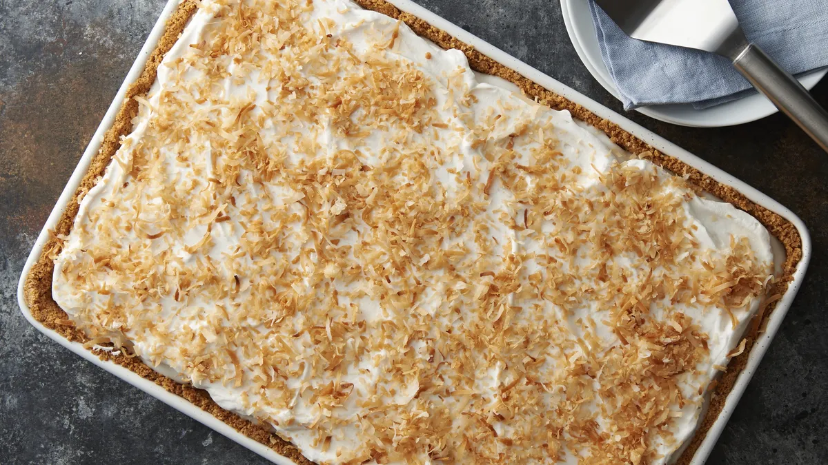 A white dish featuring a Vegan Banana-Coconut Cream Slab Pie topped with a smooth layer of coconut cream.