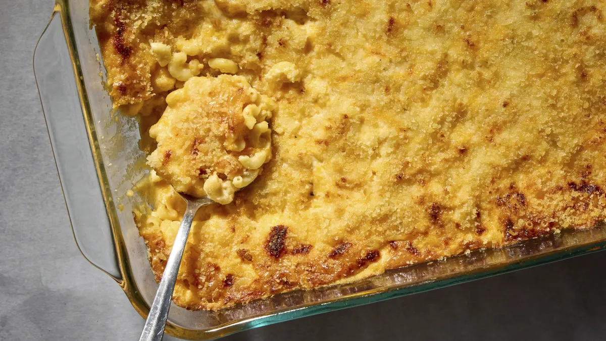 Features a close-up of a serving in a white bowl. The dish is topped with golden brown panko breadcrumbs and butter, showcasing creamy, melted cheese sauce.