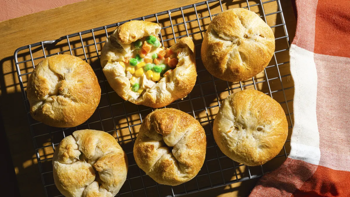 Biscuits filled with corn, carrots, peas, and condensed cream of chicken soup on top of a cooling rack with a wooden board underneath. A plaid towel is to the right of the rack.