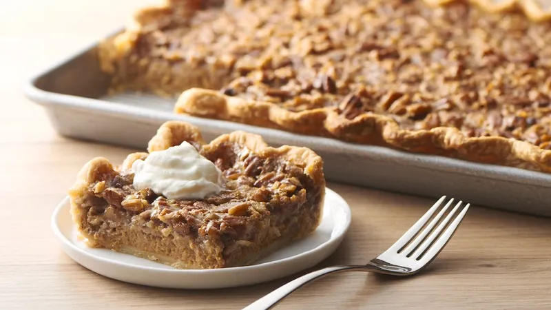 A baking sheet with pre-cut pumpkin-pecan slab pie bar squares. A white plate has a slab pie bar with whipped cream on top and a fork next to it.