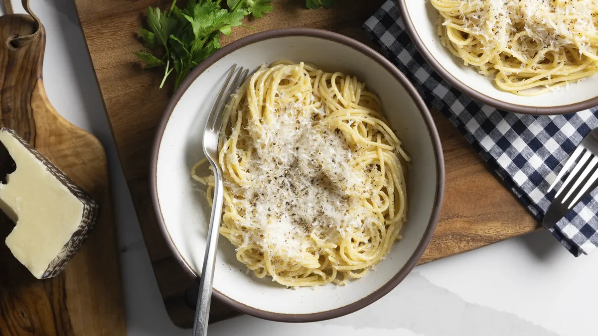 A bowl of spaghetti with cheese and pepper.