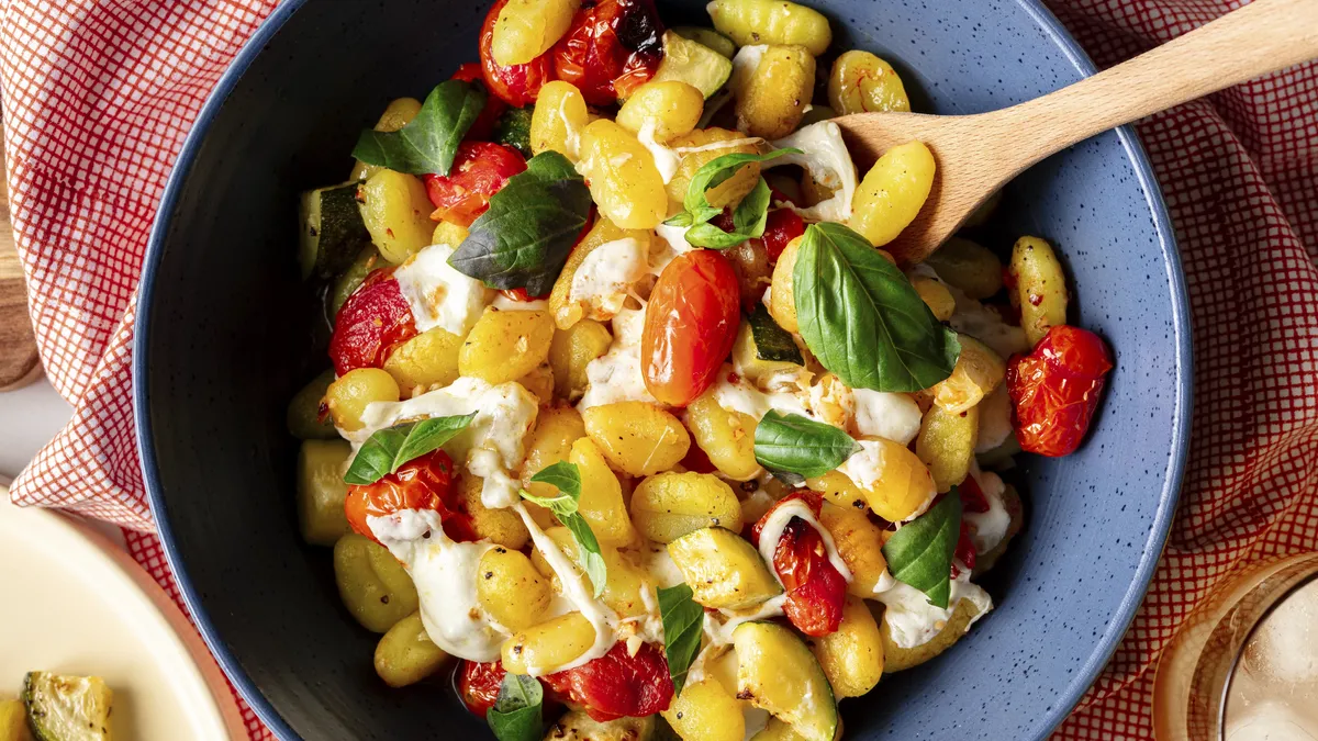 Bowl of gnocchi with cherry tomatoes, basil and cheese made on a sheet pan.