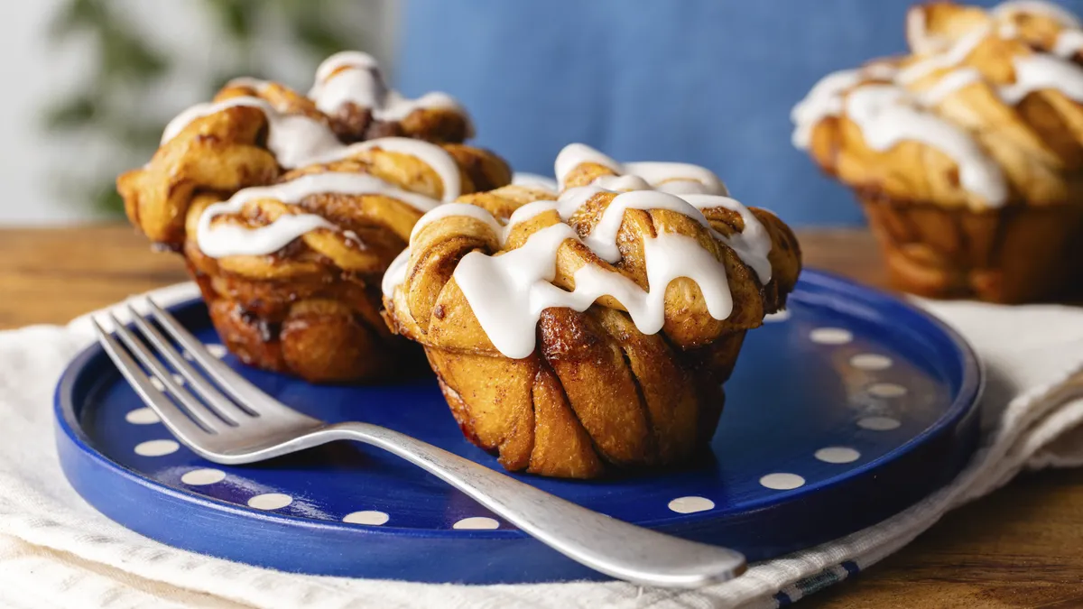 Cinnamon roll muffins drizzled with icing on a plate with a fork on the side.