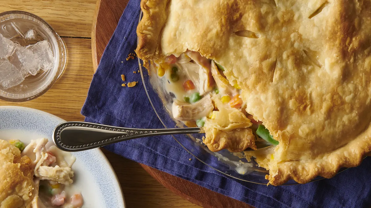 A pot pie with a golden crust and a serving spoon inside, showing a vegetable filling.
