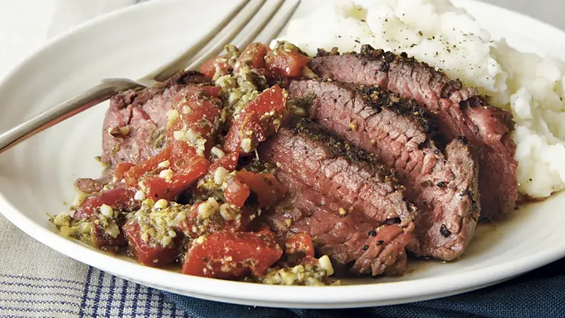 A plate of pepper steak served with roasted red pepper pesto and a variety of colorful vegetables.