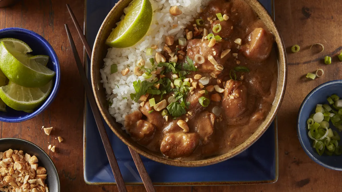 A bowl of rice and meat stew with lime, peanuts, and green onions.