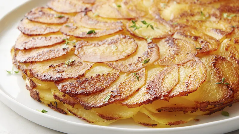 Layered thinly sliced potatoes with a crispy top on a white plate