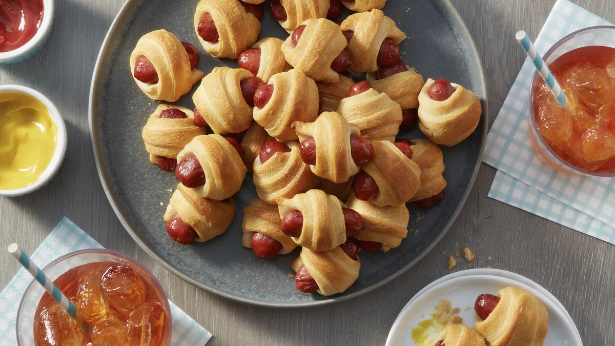 A plate of pigs in a blanket with dipping sauces.