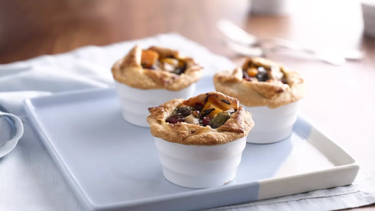 Three white round dishes with a pastry border and surrounding a filling of cranberry, butternut squash, turkey, wild rice and herbs.