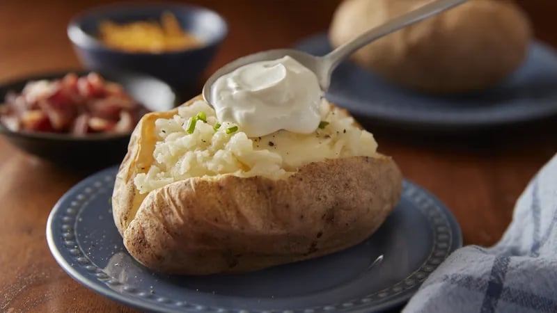 A baked potato topped with sour cream graces a blue plate, capturing the essence of classic baked potatoes.