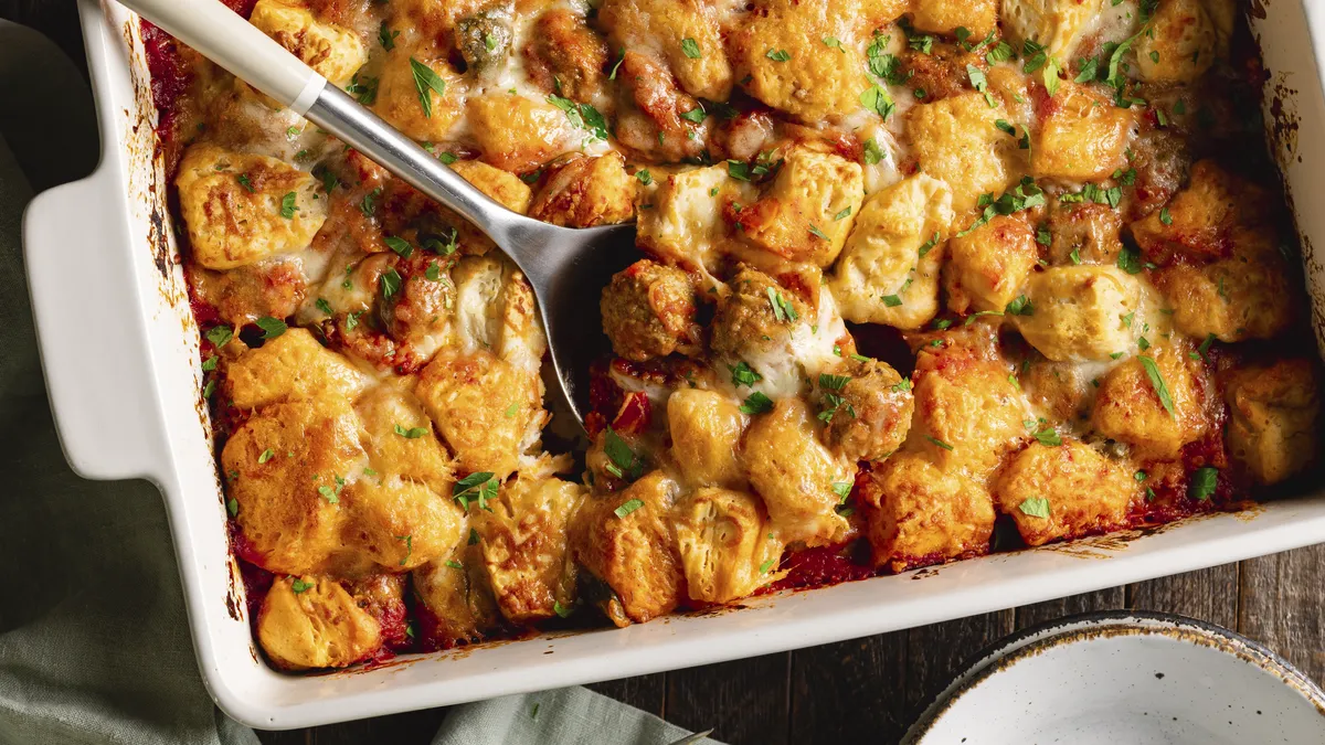 Golden-brown tater tot casserole in a white baking dish, topped with melted cheese and green herbs.