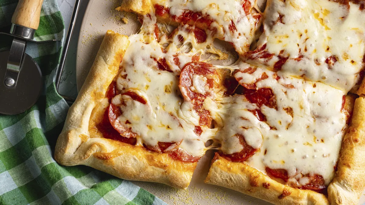 Close-up of a cheesy pepperoni pizza with thick crust, cut into squares.